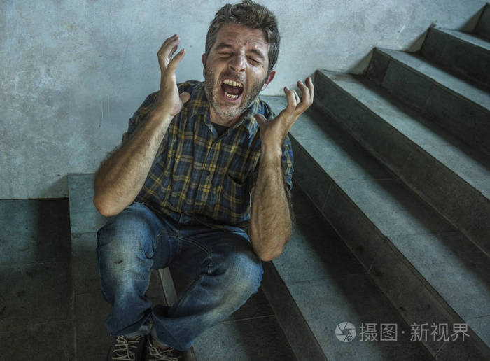 年轻的抑郁和偏执的男人坐在黑暗肮脏的街道拐角楼梯