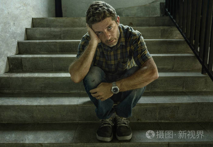 绝望的男人坐在户外黑暗肮脏的街角楼梯上感到不舒服