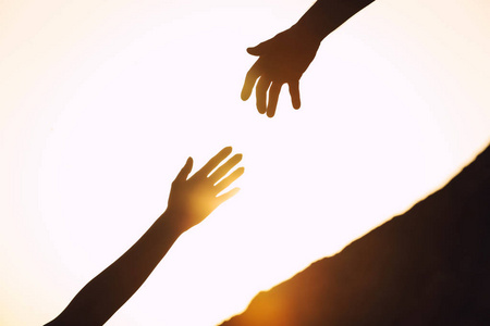 男人和女人在夕阳下互相帮助爬山的剪影,特写照片