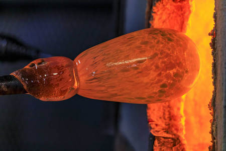 玻璃吹风机在玻璃制造厂的窑炉中加热棒上熔化的玻璃气泡照片