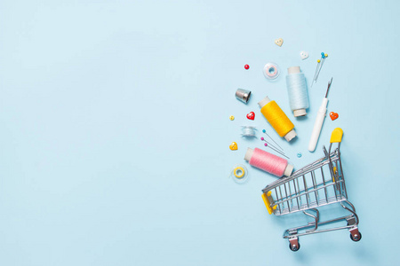 带蓝色背景缝纫配件的超市购物车,缝线,刺绣.文本空间,平放,俯视图.