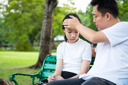 父亲抚摸可爱小女孩的额头,检查体温,关心父亲照顾生病的女儿,在户外