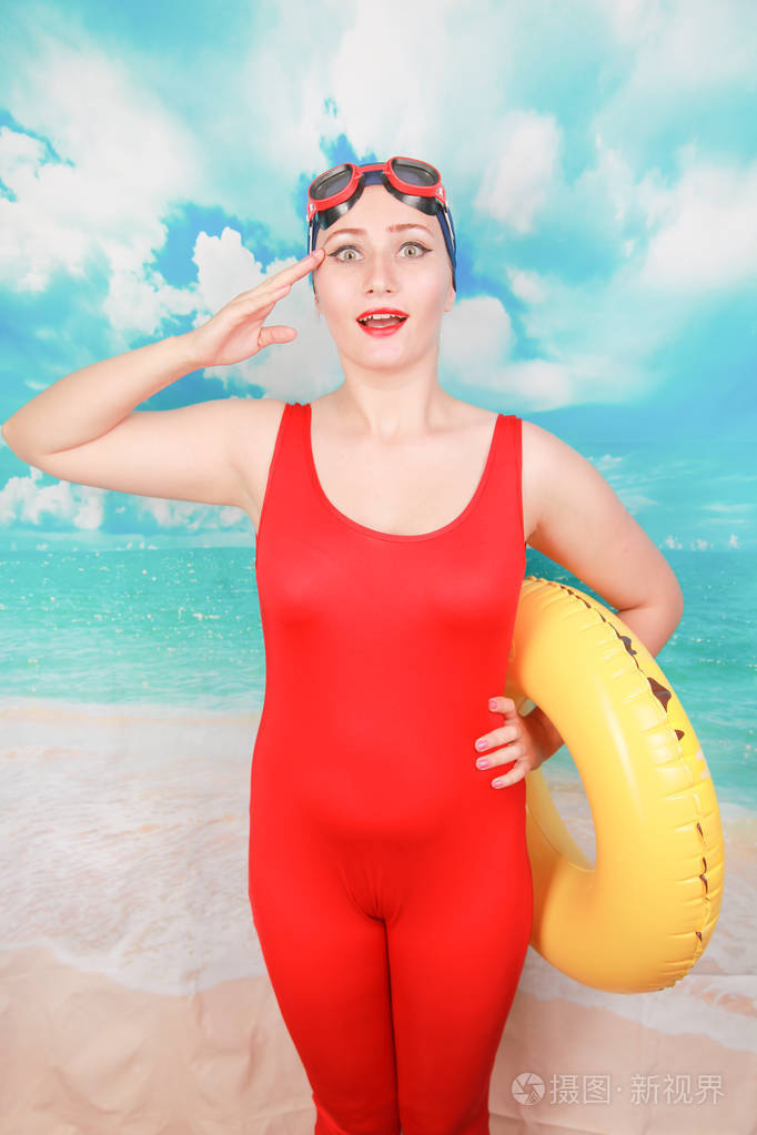 摄影棚拍摄的美女性感女子穿着红色复古泳装在蓝天背景上手持生命戒指