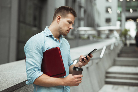 一位年轻英俊的上班族在午休时间站在街上检查他的手提电脑和一杯咖啡