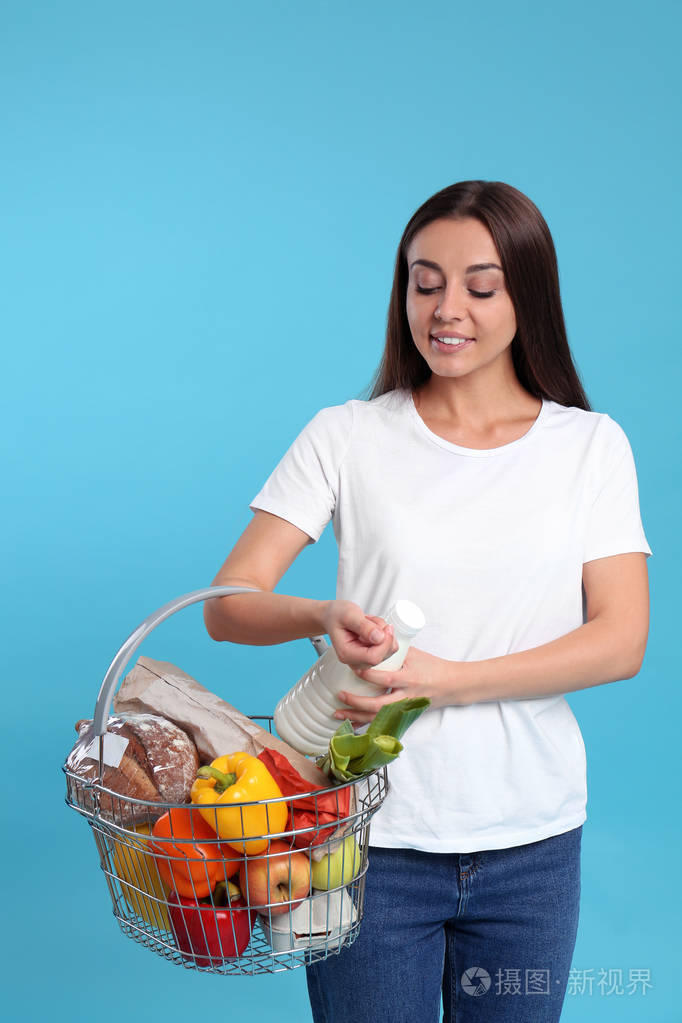 蓝色背景下拿着装满商品的购物篮的年轻女子