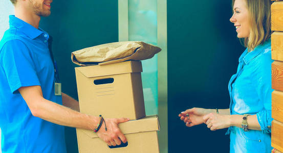 身着蓝色制服的微笑送货员将包裹箱递送给收件人-快递服务理念照片
