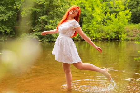 河边玩水快乐的红发女人穿着白色的裙子在河边嬉戏,在夏天泼水.