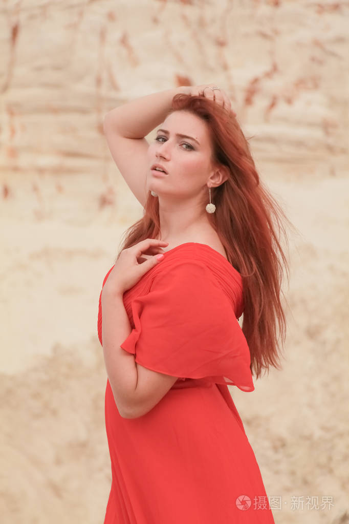 年轻美丽的白种女人穿着红色长裙在沙漠中与沙子合影