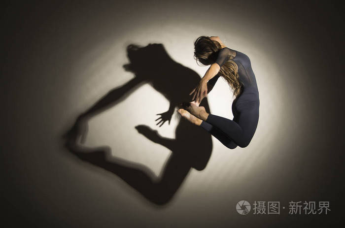 女孩在黑暗中表演跳高体操在白色的背景上有一个形状的影子