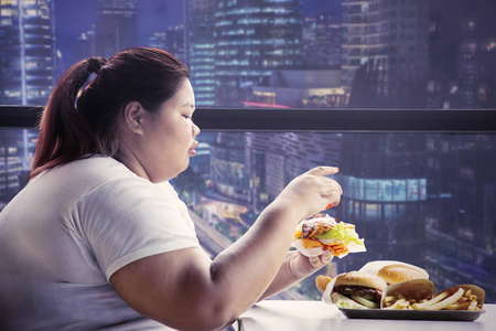 肥胖妇女晚上在咖啡馆吃垃圾食品照片