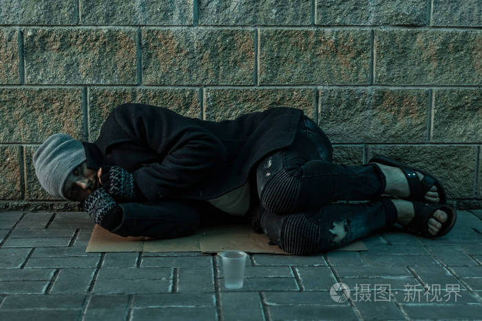 一个无家可归的男人睡在街上冰冷的地板上手上挂着求助标志无家可归者