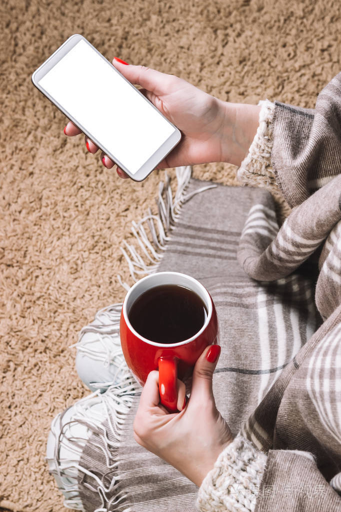 一位年轻女子坐在地毯上,手里拿着一部手机.