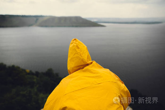 穿着黄色雨衣的时髦旅行者站在悬崖上观望