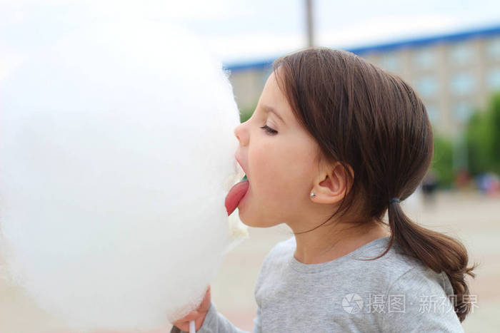 在一个城市庆典上梳着辫子的小女孩试图咬一个大棉花糖球