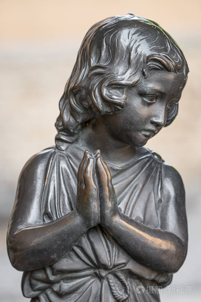 一个美丽的小女孩在市中心公园祈祷的老雕像