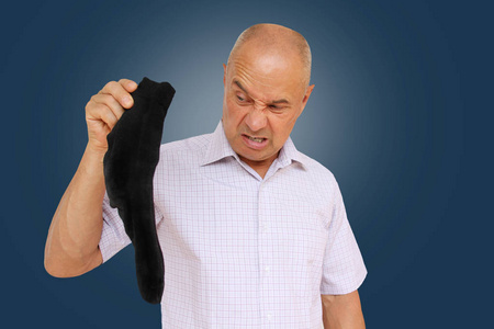 男人穿袜子一个穿浅色衬衫的男人手里拿着黑袜子闻了闻,脸上的臭味让