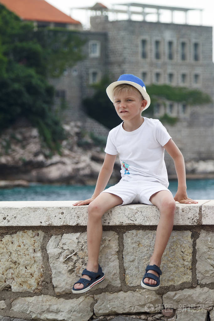 一个戴蓝帽子的男孩把腿叠在栏杆上坐着