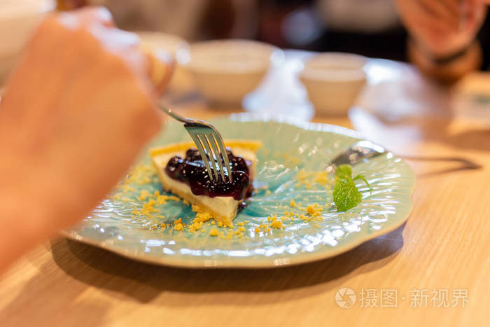 女的手拿叉子在餐厅吃蓝莓奶酪蛋糕