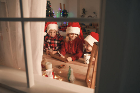 小孩在窗口可爱的小孩子在家里给圣诞老人写信.通过窗口查看照片