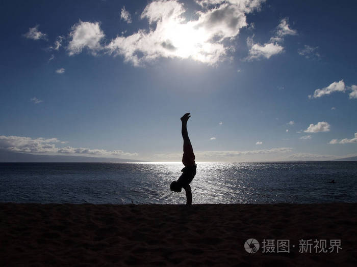 夕阳下空旷海滩上男人倒立的剪影