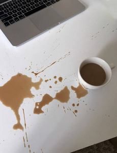 咖啡洒出来的一大块污渍.在桌上白色桌面上的笔记本电脑旁.照片