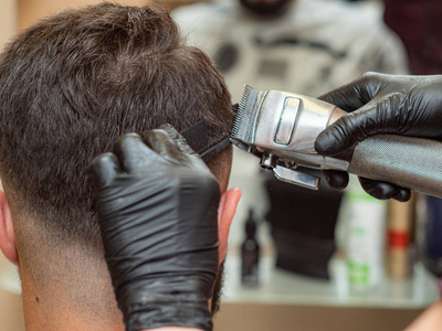 大师手戴黑色橡胶手套在理发店做现代发型选择性软聚焦背景模糊