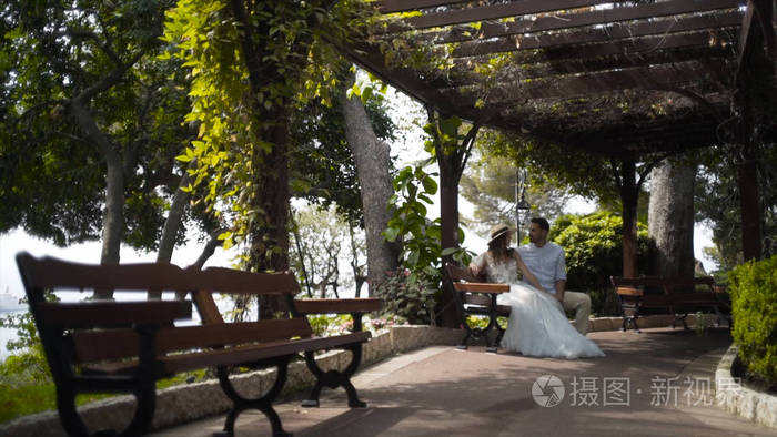 蜜月里坐在凉亭里的一对美丽的情侣.丈夫亲吻他珍贵妻子的脸颊.