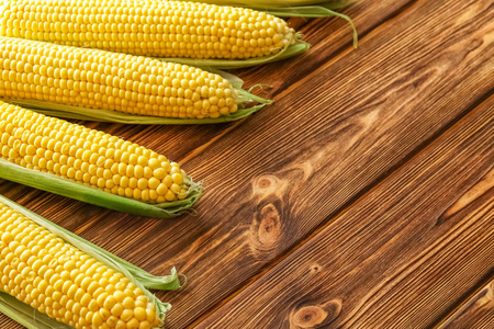 成熟的,甜的,新鲜的玉米棒,特写在一个棕色的乡村木桌上.照片