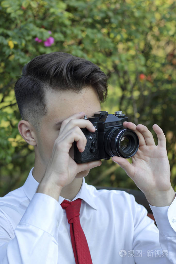 穿着时髦的年轻人坐在公园里拍照他手里拿着一台单反胶卷相机