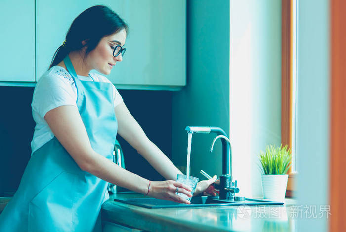 人手拿着玻璃杯在厨房的水龙头上倒水