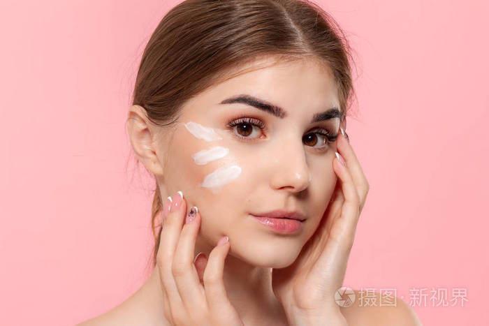 这个漂亮的模特把透明质酸乳霜的白色管夹在粉红色的背景上,给皮肤涂