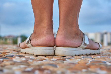 凉鞋海穿着白色凉鞋的女性双腿站在铺着海石的人行道上照片