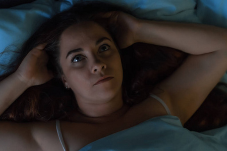 年轻的紧张或抑郁的女人躺在床上用手抓着头,睡不着.失眠概念照片