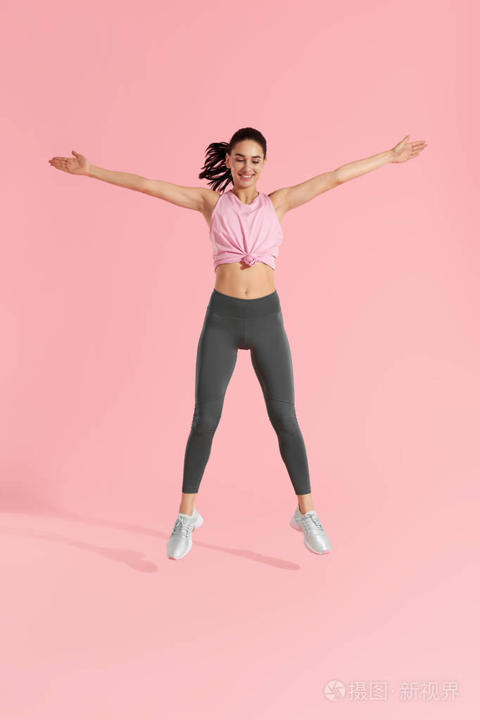 健身跳跃。在粉红色背景上做跳跃运动的女人