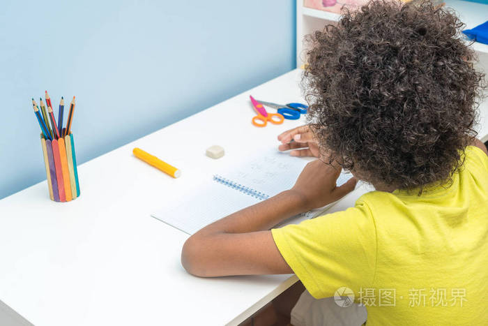 男孩坐在家里做作业的后视图黑人男孩做作业教育理念
