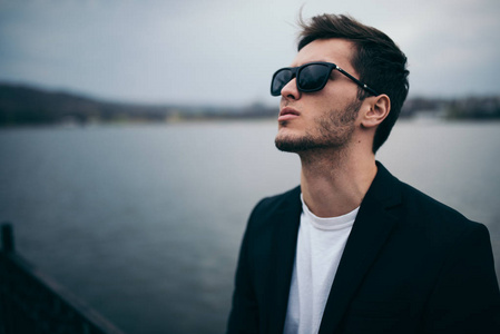 帅气,忧郁,忧郁的男人,穿着休闲套装,戴着墨镜,仰望天空,在湖面的户外