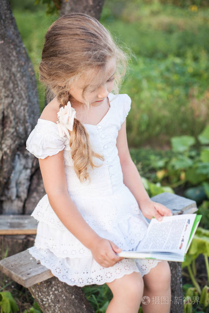 夏天一个手里拿着一本书的小女孩在草地上