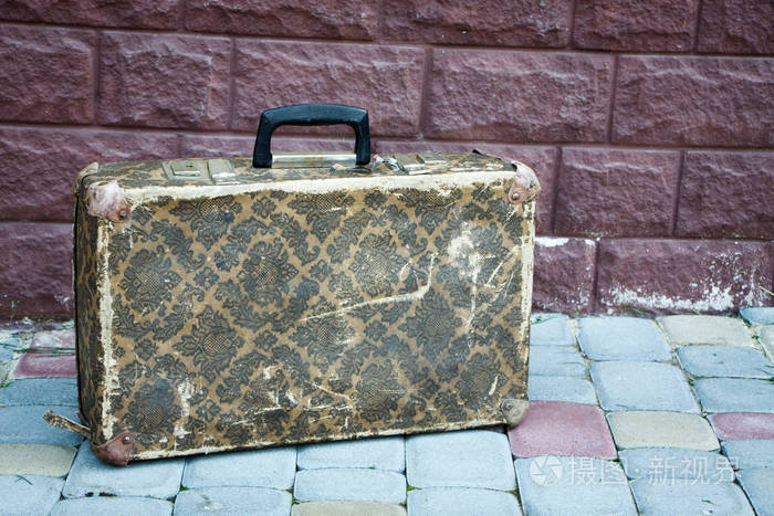 一个老式的手提箱有着有趣的图案和金属角立在砖墙背景背景或概念上