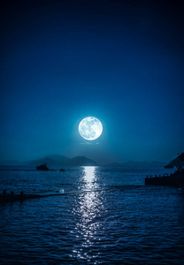 夜晚宁静海水中的小船和月亮的风景.照片