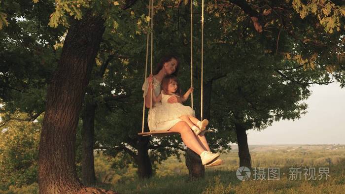 母亲和婴儿在森林里的橡树枝上荡秋千.