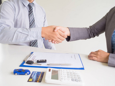 女顾客用信用卡和签了租车单的售货员,握手成交照片