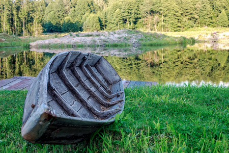 一艘小木船在岸边干涸,在平静的湖边,森林倒映在湖面上.照片