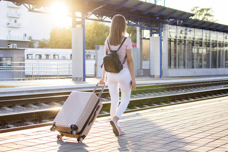 漂亮的女孩正拿着行李站在车站等火车,学生要去旅行,她正沿着月台走着