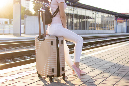 漂亮的女孩坐在火车站的行李上等火车,学生去旅行,特写照片