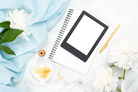 俯视电子书阅读器,纸质记事本,牡丹花,大理石背景上的彩色丝巾.