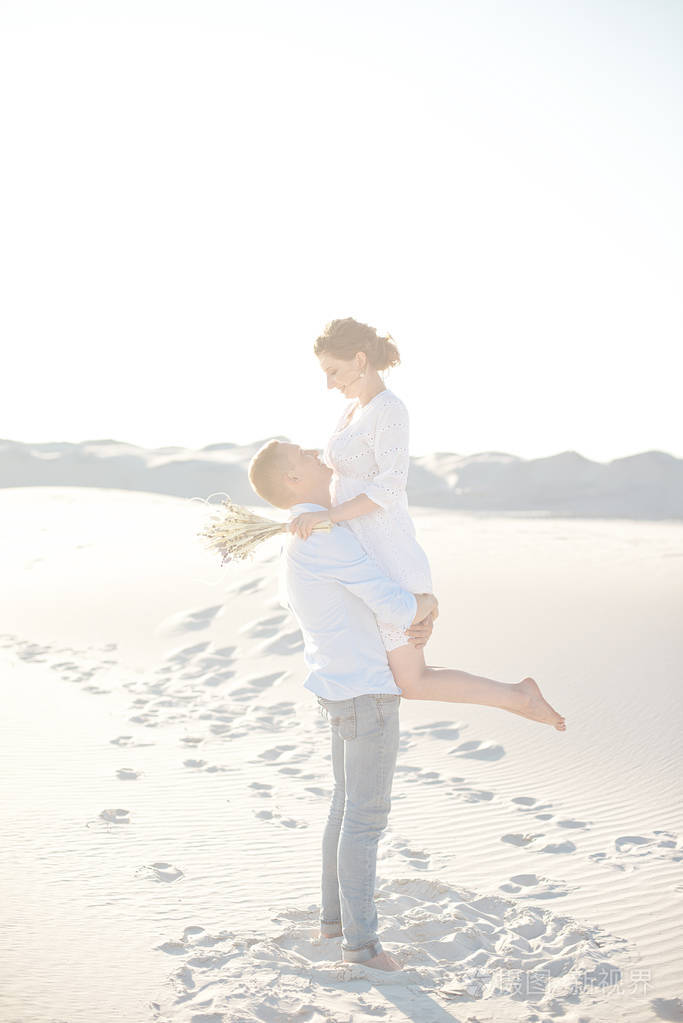 年轻夫妇在沙丘上欣赏日落那家伙抱着他的女朋友看着对方的眼睛