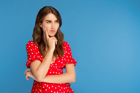 专注思考一个穿着红裙子的专注的年轻女人望向别处,在蓝色的背景下