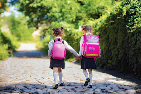 一个两个女生背着背包在小学外的背影.孩子们放学回家.研究结束.