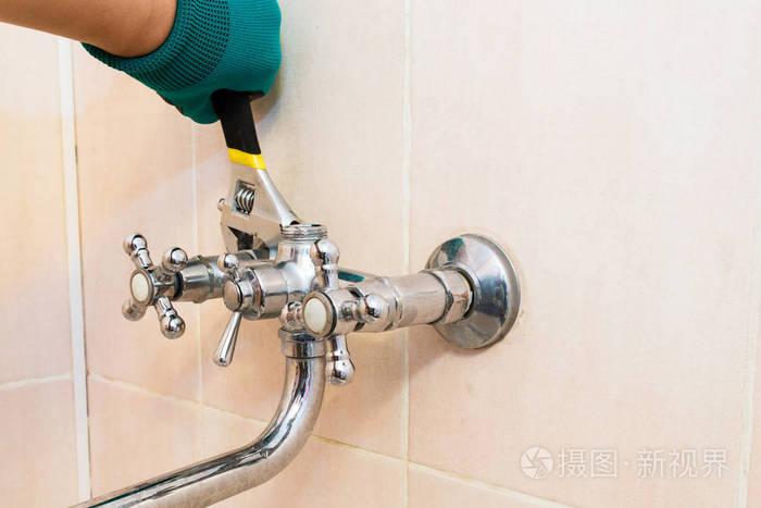一只戴着手套的手拿着扳手修理浴室的水龙头