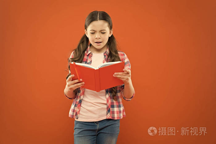 可爱的小孩在橙色背景上看书.可爱的小女孩为了好玩而读书.